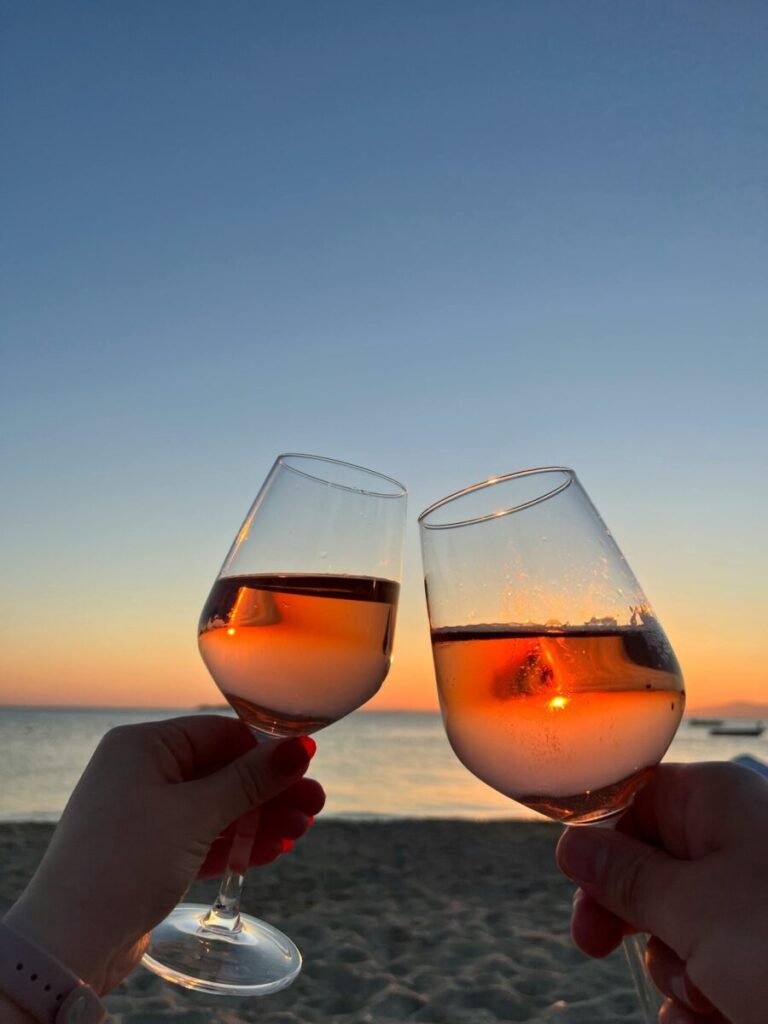 Two glasses of wine clinking at sunset on Avşa Beach, Türkiye, creating a romantic seaside vibe.